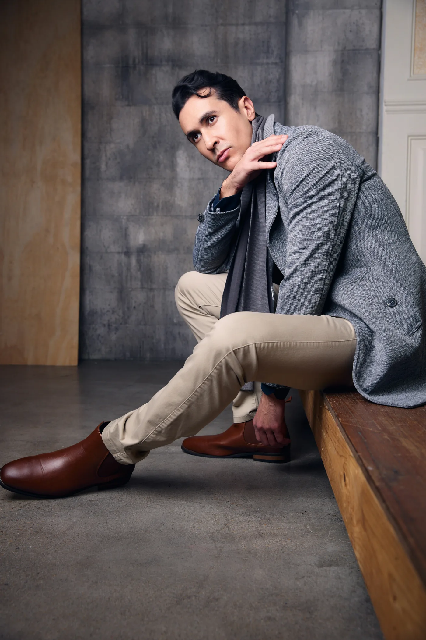 A man in a slate blazer and beige trousers crouching on a wooden platform
