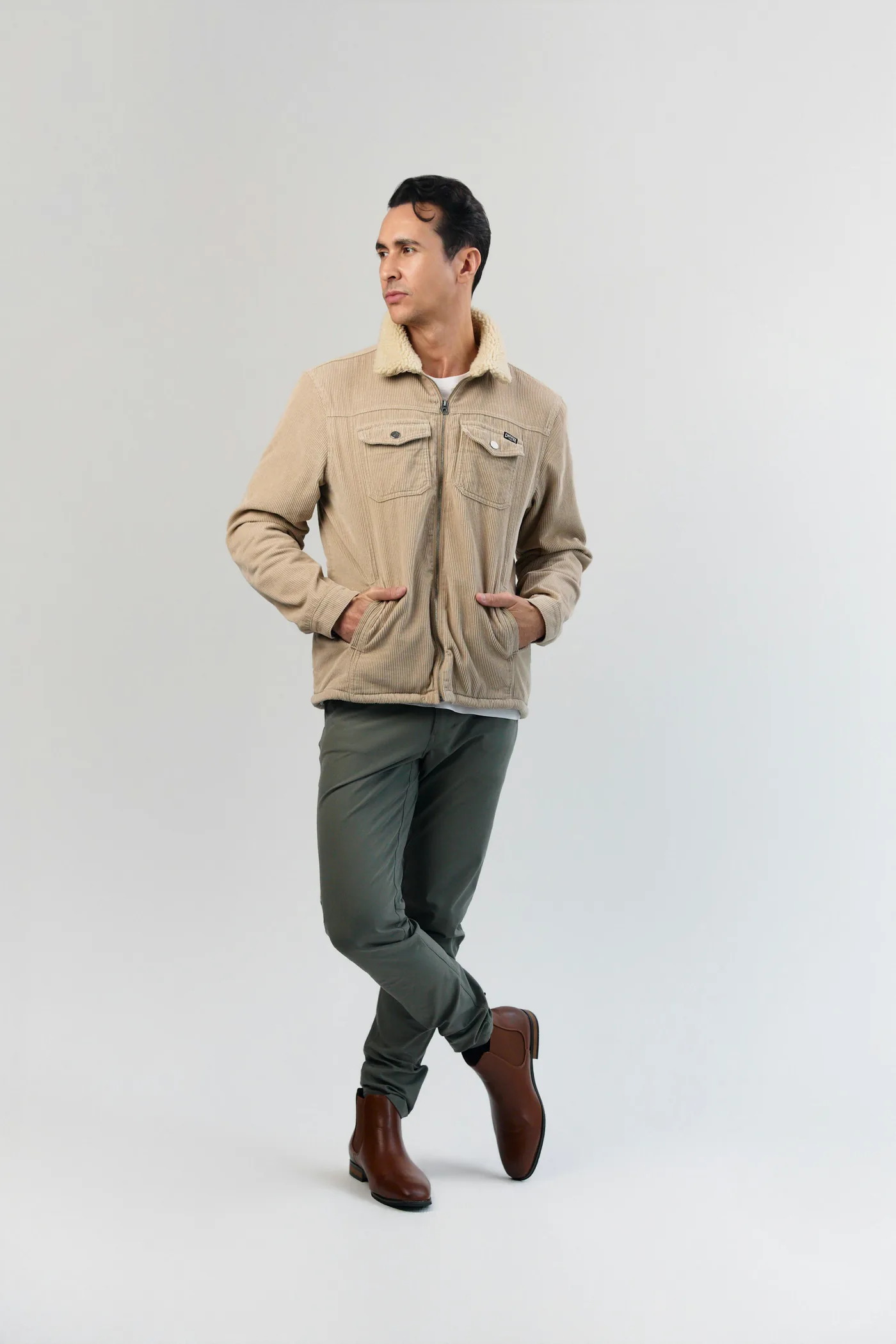 A man in a sand corduroy jacket, olive trousers and brown leather boots