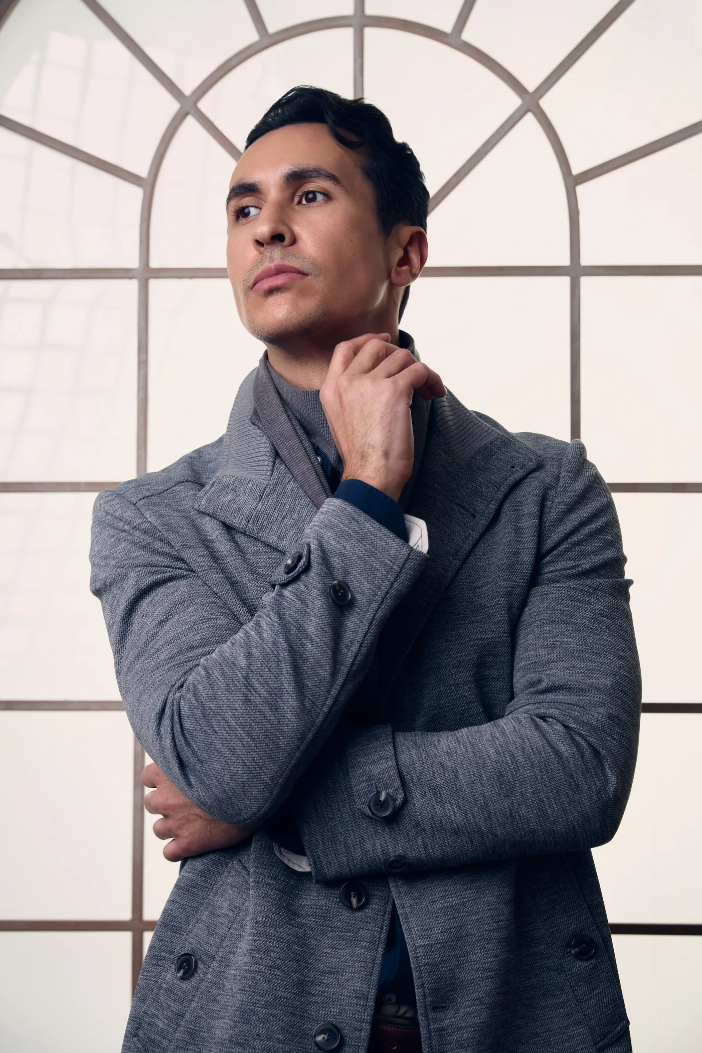 A man in a grey coat and scarf in front of a large arched window