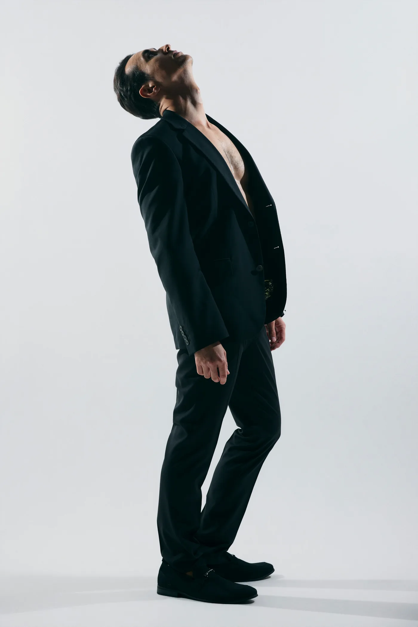 A man in a black suit with his head tilted back