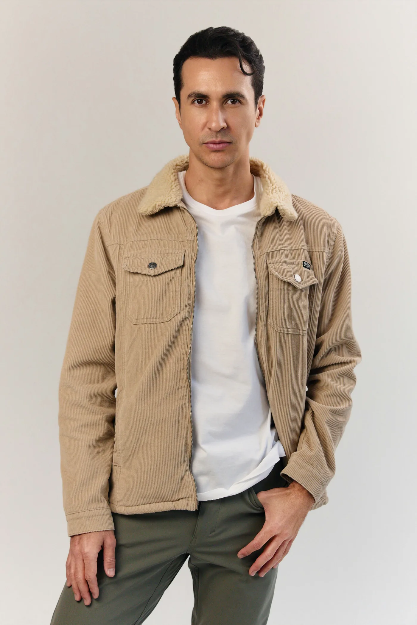 A man in a tan corduroy jacket with a sherpa collar over a white T-shirt